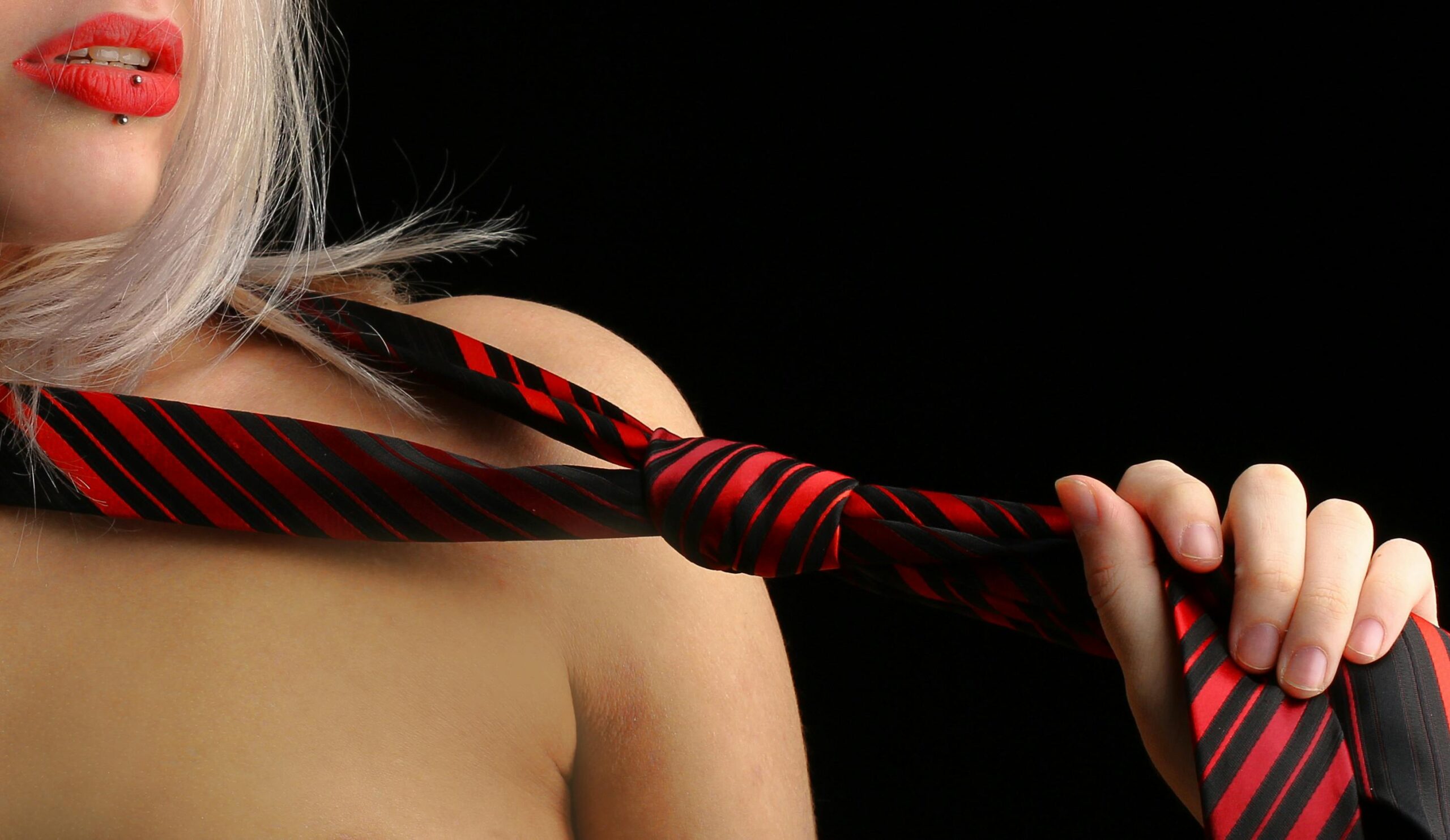 Close-up of a woman holding a red and black necktie, emphasizing sensuality and style.